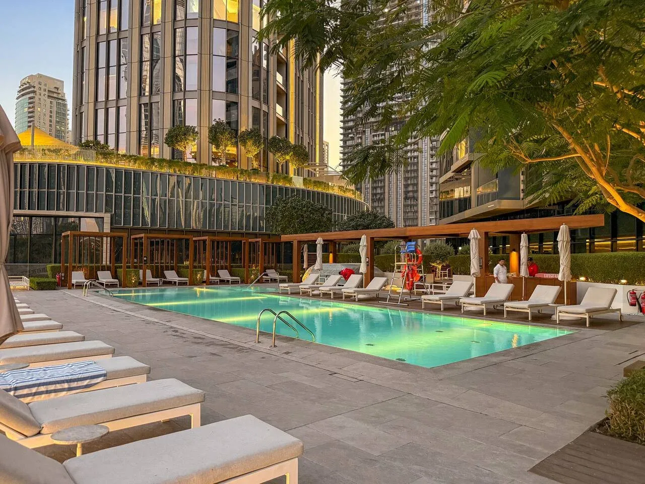 An outdoor swimming pool is surrounded by lounge seating and tall buildings.
