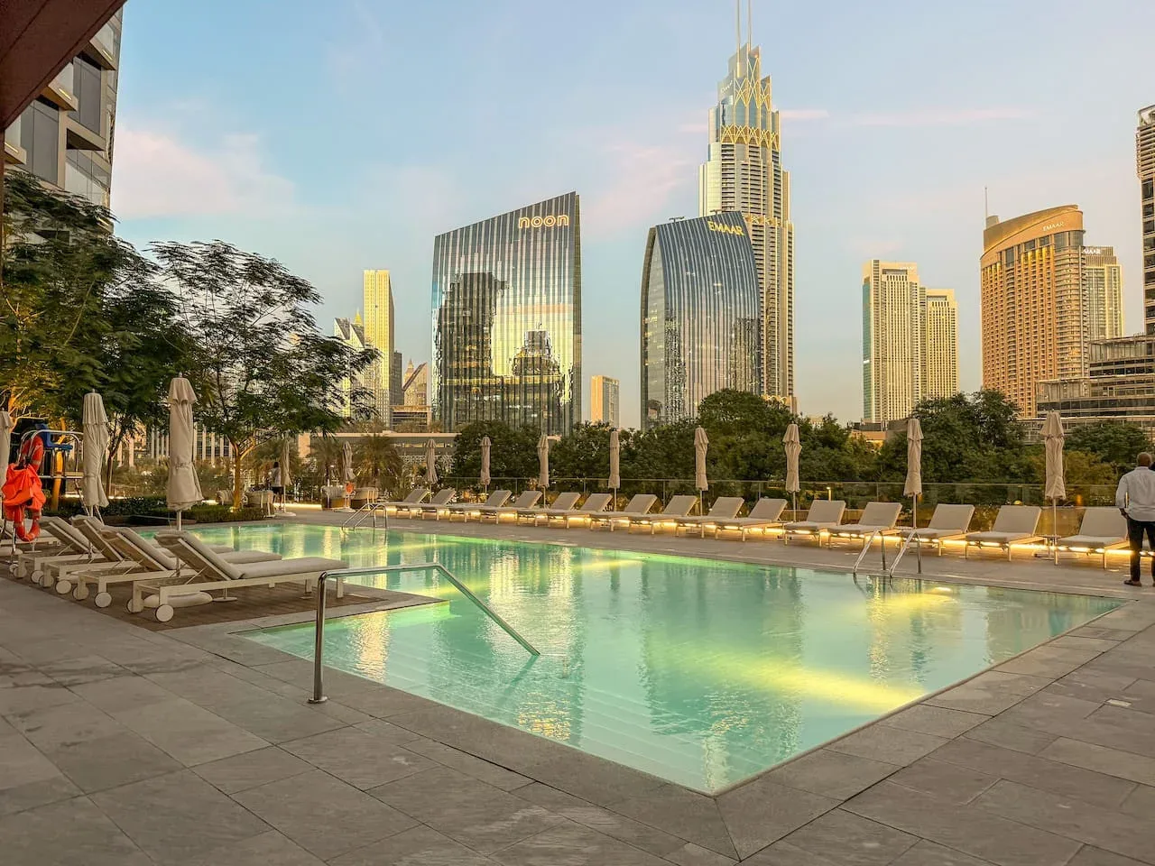 An outdoor swimming pool is surrounded by lounge seating and tall city buildings.