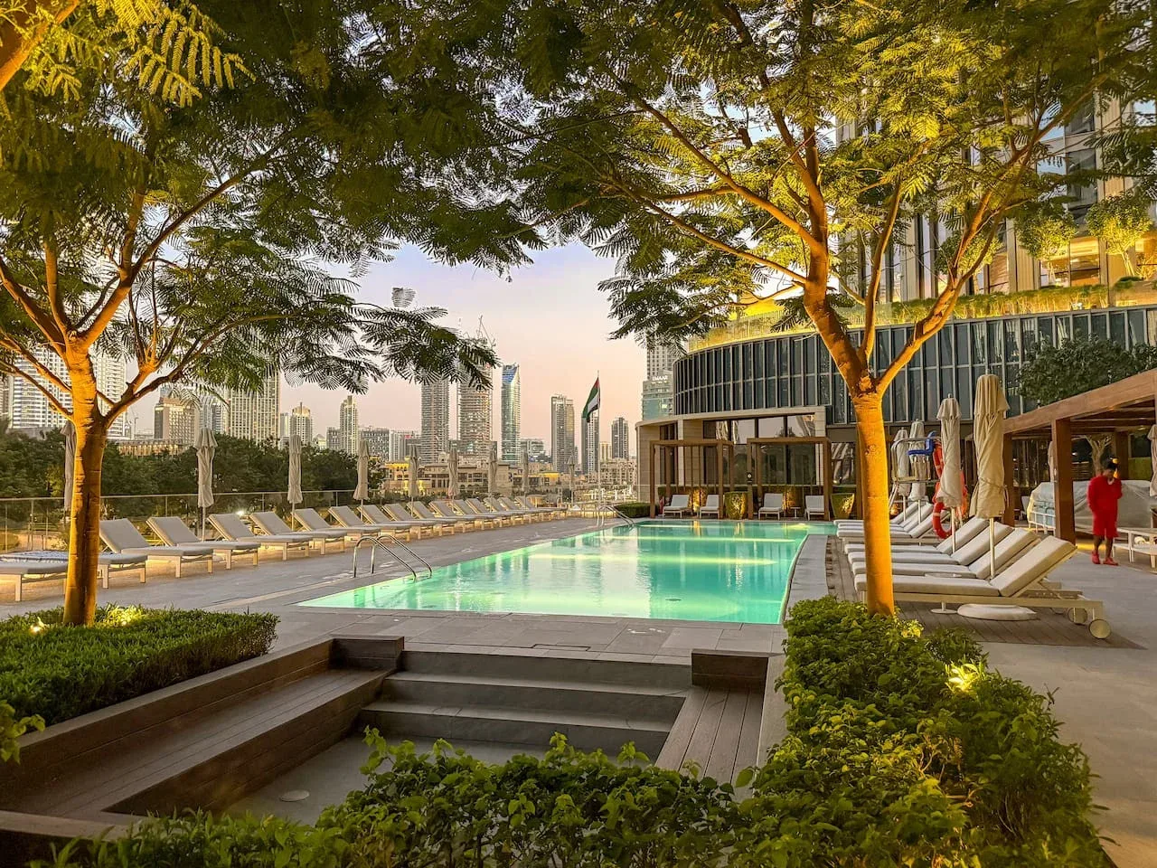 An outdoor swimming pool is surrounded by lounge seating and leafy trees.