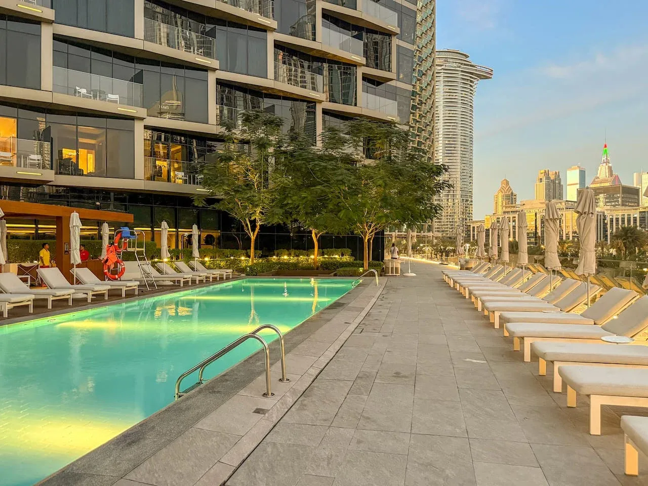 A rooftop pool and sun loungers overlook a city skyline.