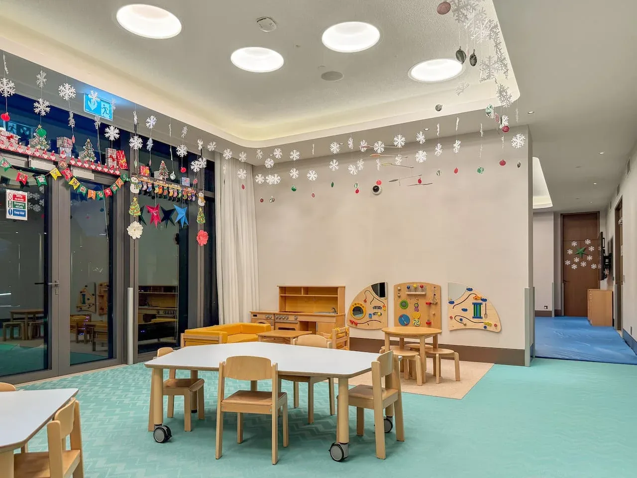A children’s playroom with small tables, chairs, and colorful wall activity panels.