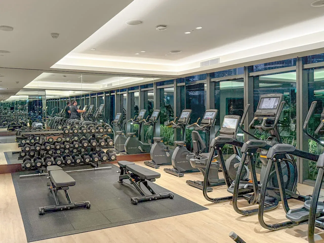 A gym with rows of cardio machines, weight equipment, and a mirrored wall.