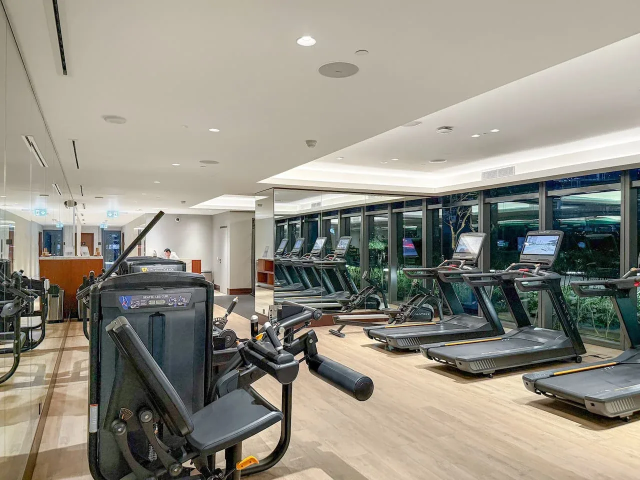 A fitness room with exercise machines and treadmills beside large windows.