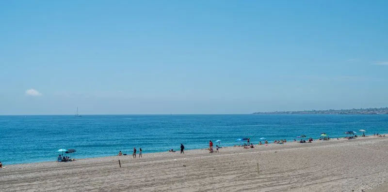 A sandy beach stretches beside calm blue water under a clear sky.