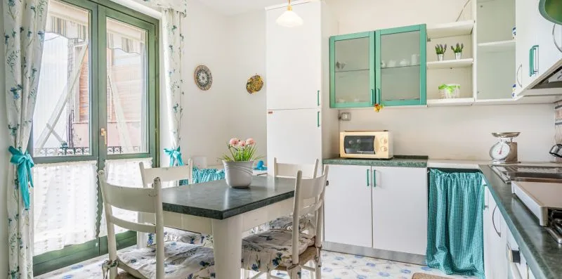 A bright kitchen with a dining table beside green-framed windows.