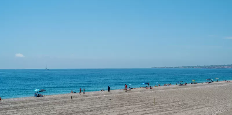 A sandy beach stretches beside the blue sea under a clear sky.