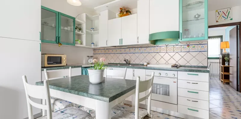A bright kitchen with white cabinets, a tiled backsplash, and a dining table.