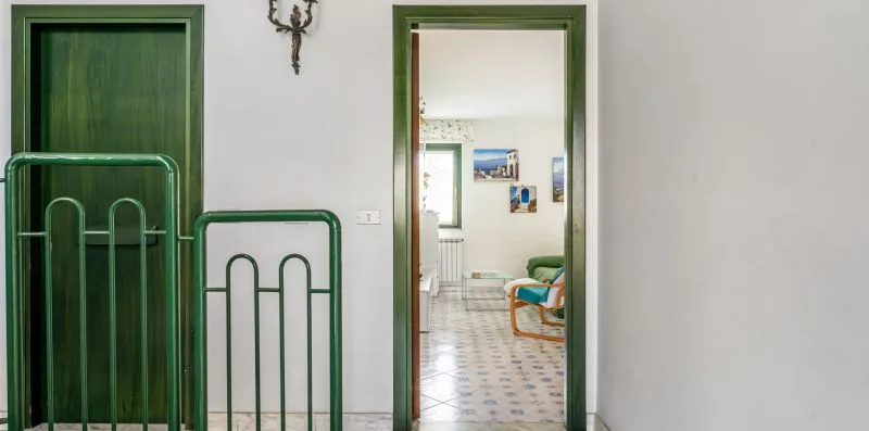 A hallway with green metal gates opens into a bright sitting area.