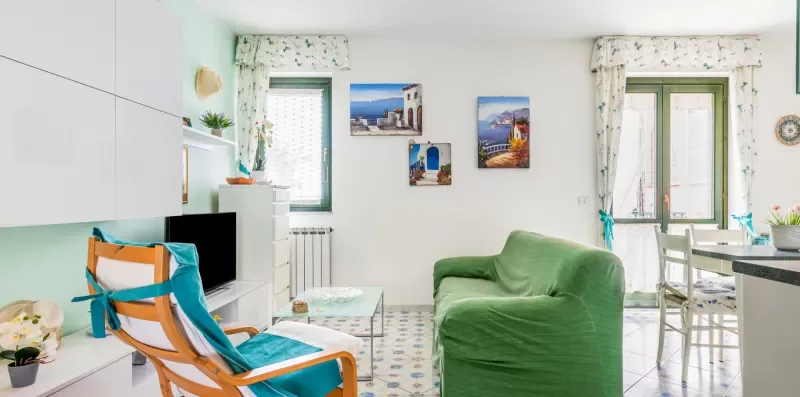 A bright living room with green seating, a television, and windows.