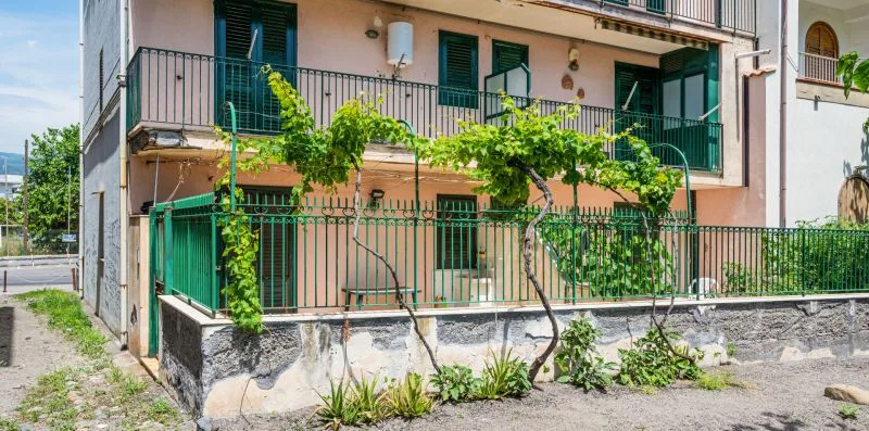 A pink residential building with balconies and green climbing vines along the railings.