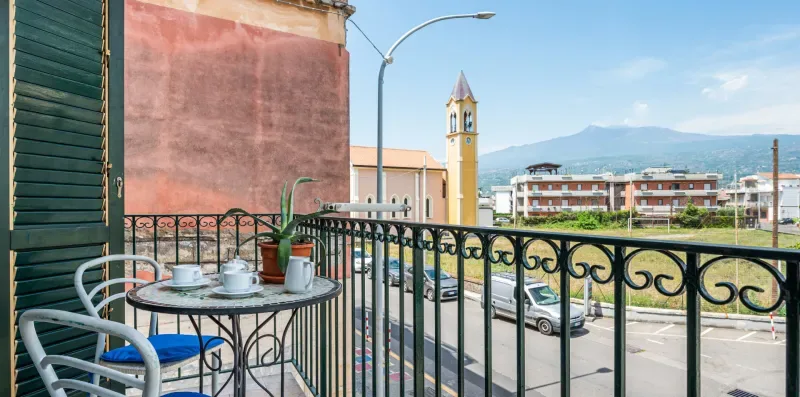 A balcony with outdoor seating overlooks a street and distant mountains.