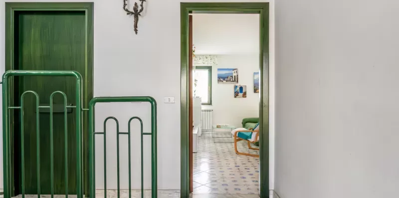 A green-trimmed doorway opens onto a bright room with seating and wall art.