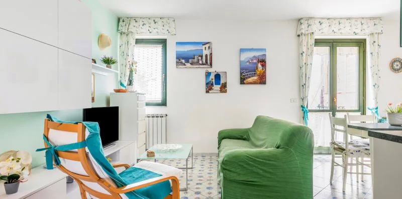 A bright living room with green seating, a television, and windows.