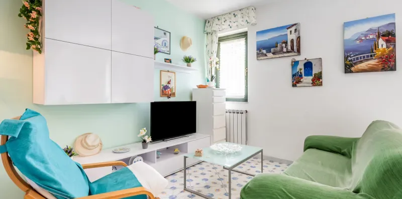 A living room with green seating, a television, and framed wall art.