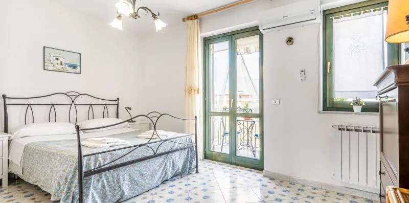A bright bedroom with a metal bed beside green-framed glass doors.