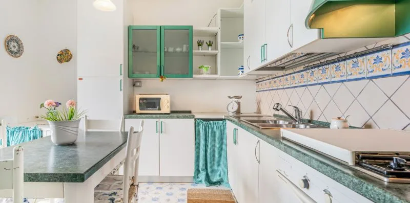 A bright kitchen with green cabinetry, tiled walls, and a countertop.