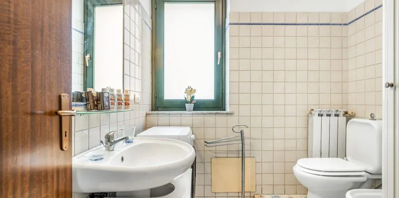 A tiled bathroom with a sink, toilet, and window.