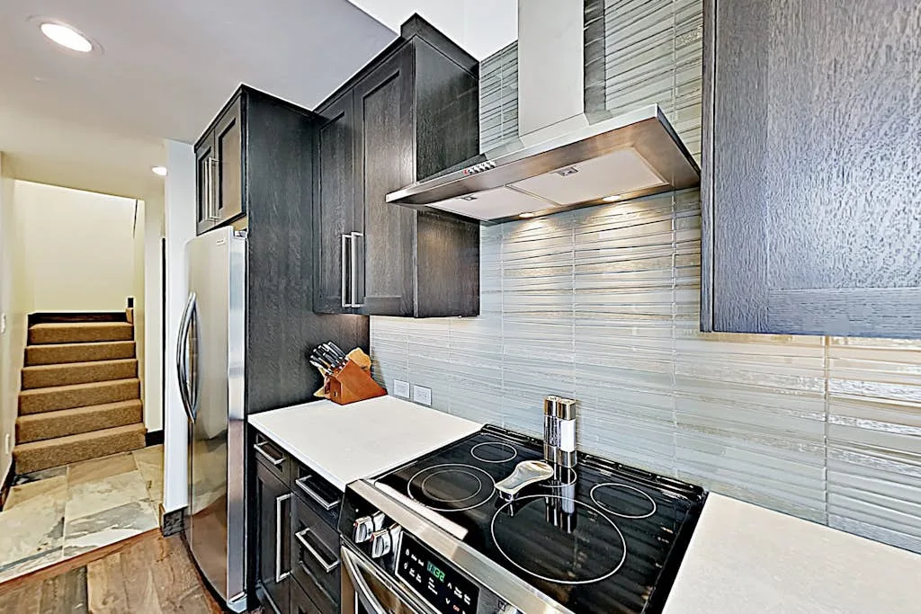 A modern kitchen with dark cabinets, a countertop, and a cooktop.