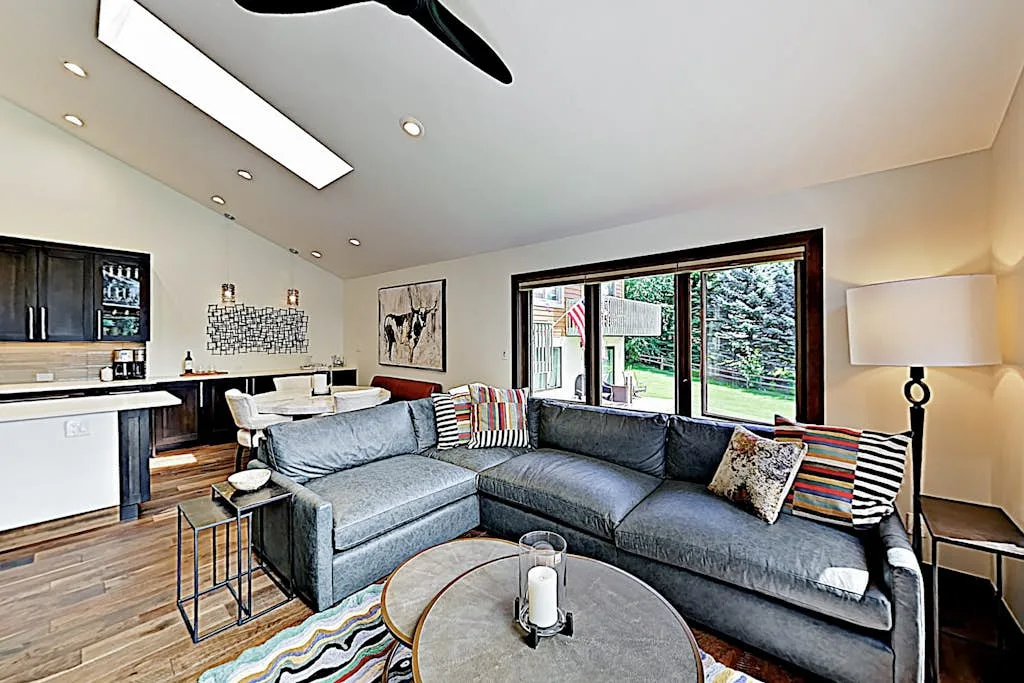 Living room with gray sectional seating and a large window overlooking greenery.