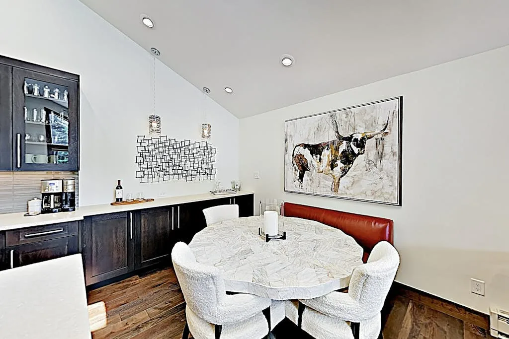 A dining area with a round table, upholstered seating, and a large wall painting.