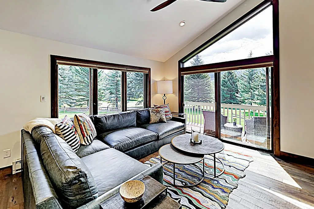 A bright living room with a sectional sofa beside large windows opening onto a deck.