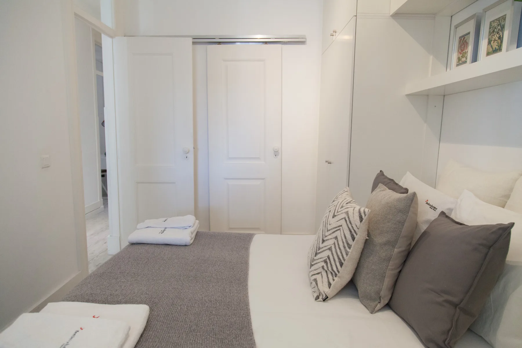 Un dormitorio con una cama, ropa de cama gris y almohadas junto a un armario blanco.