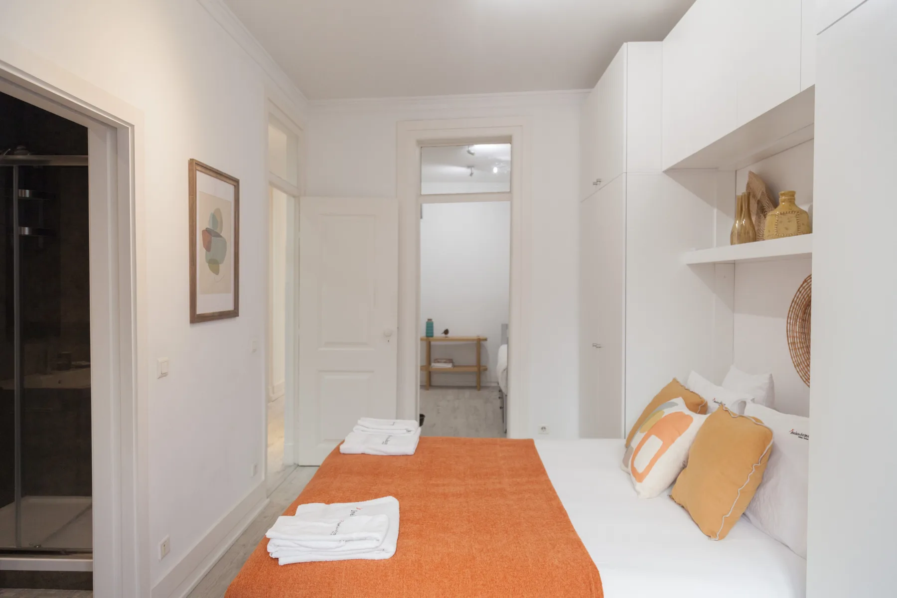Un dormitorio luminoso con ropa de cama naranja y estantes blancos empotrados.