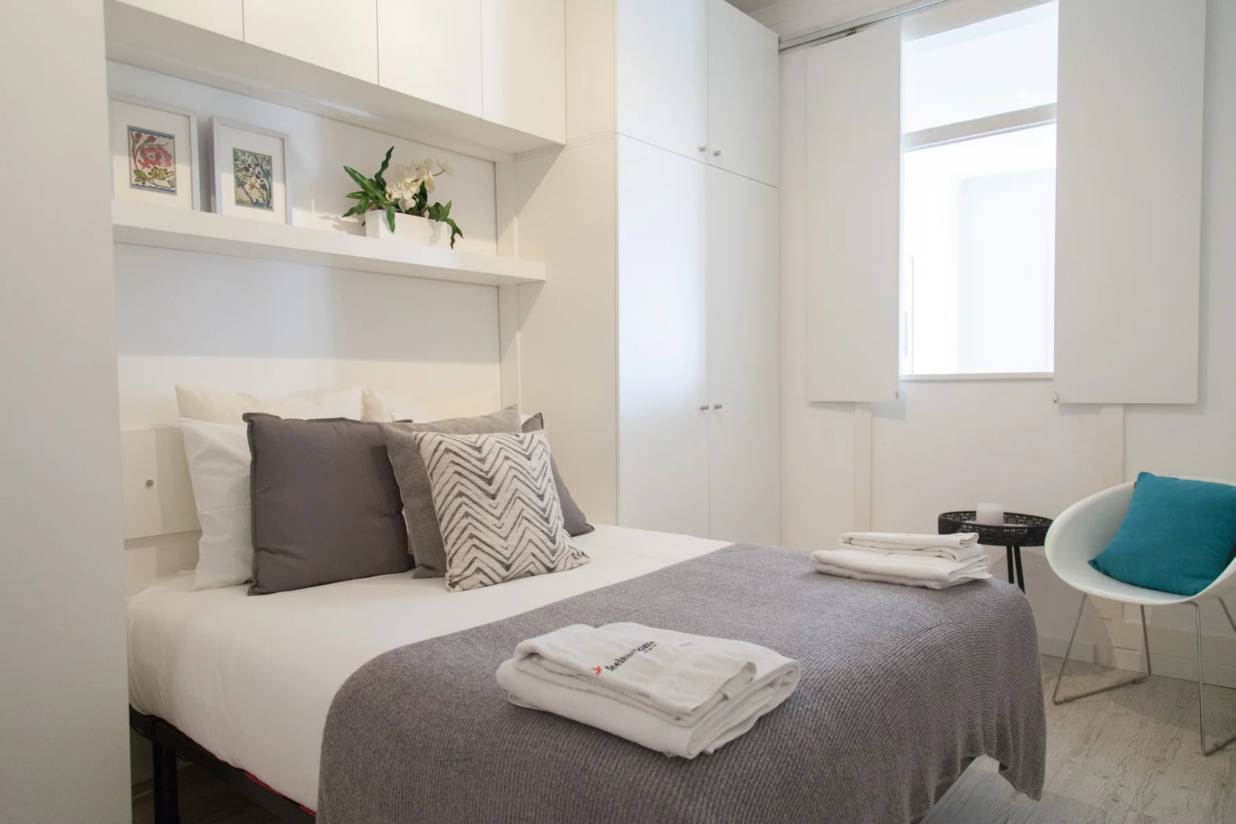 Un dormitorio luminoso con una cama bien hecha y estantes en la pared.