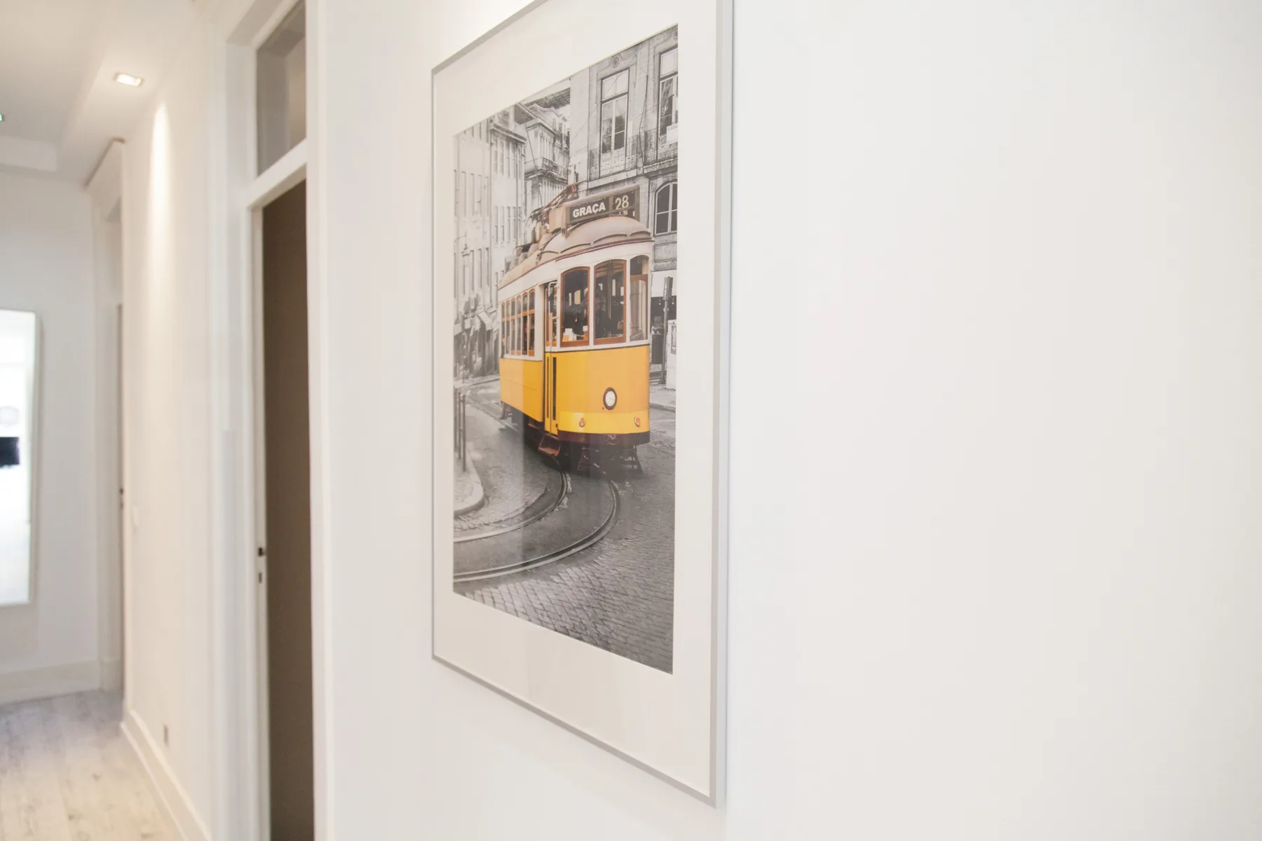 Un pasillo con una lámina enmarcada de un tranvía amarillo en la pared.