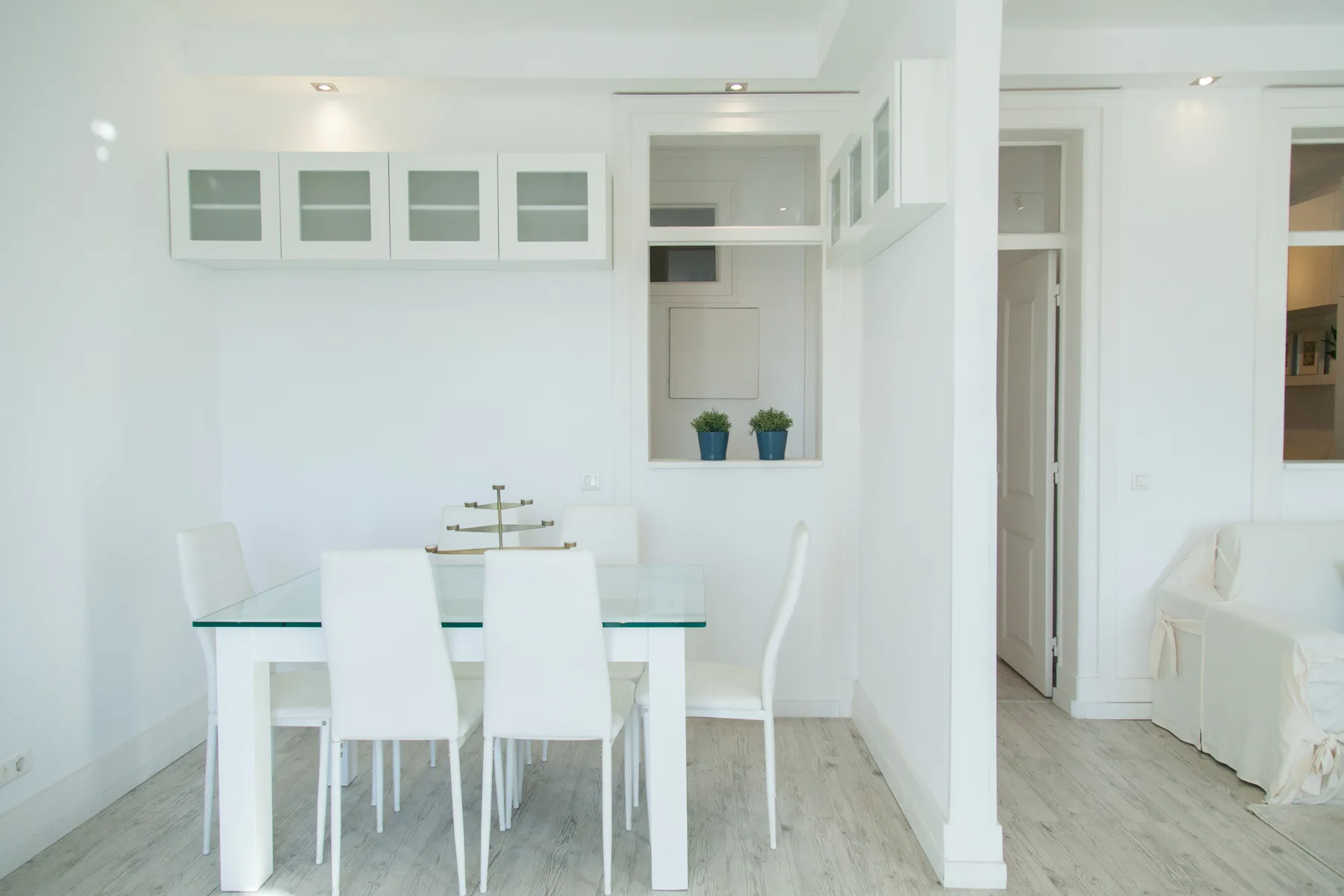 Un comedor luminoso con una mesa de vidrio y asientos blancos.