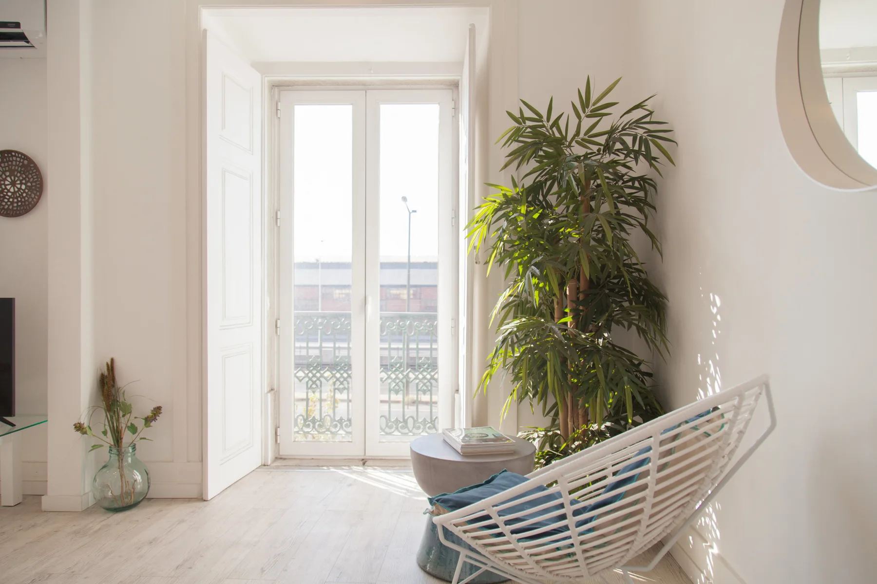Una luminosa sala de estar con una silla blanca de tejido abierto y plantas frondosas.