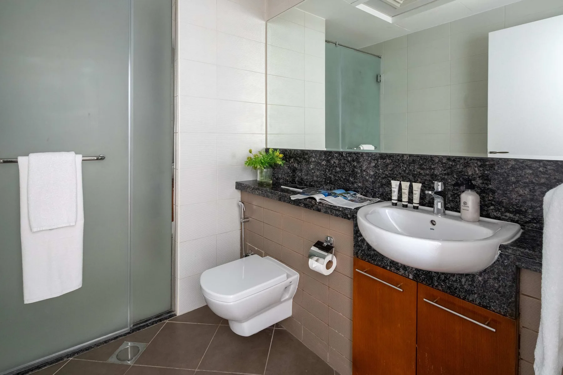 A tiled bathroom with a glass shower, wall-mounted toilet, and sink vanity.