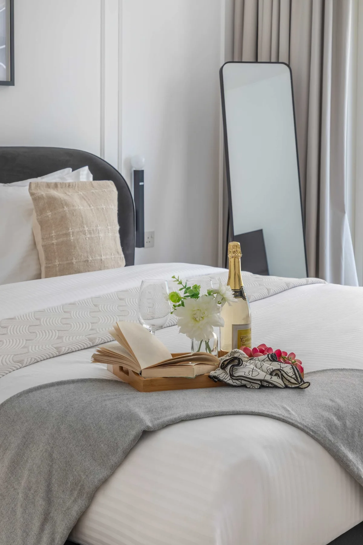 A neatly made bed with an open book, flowers, and a bottle arranged on top.