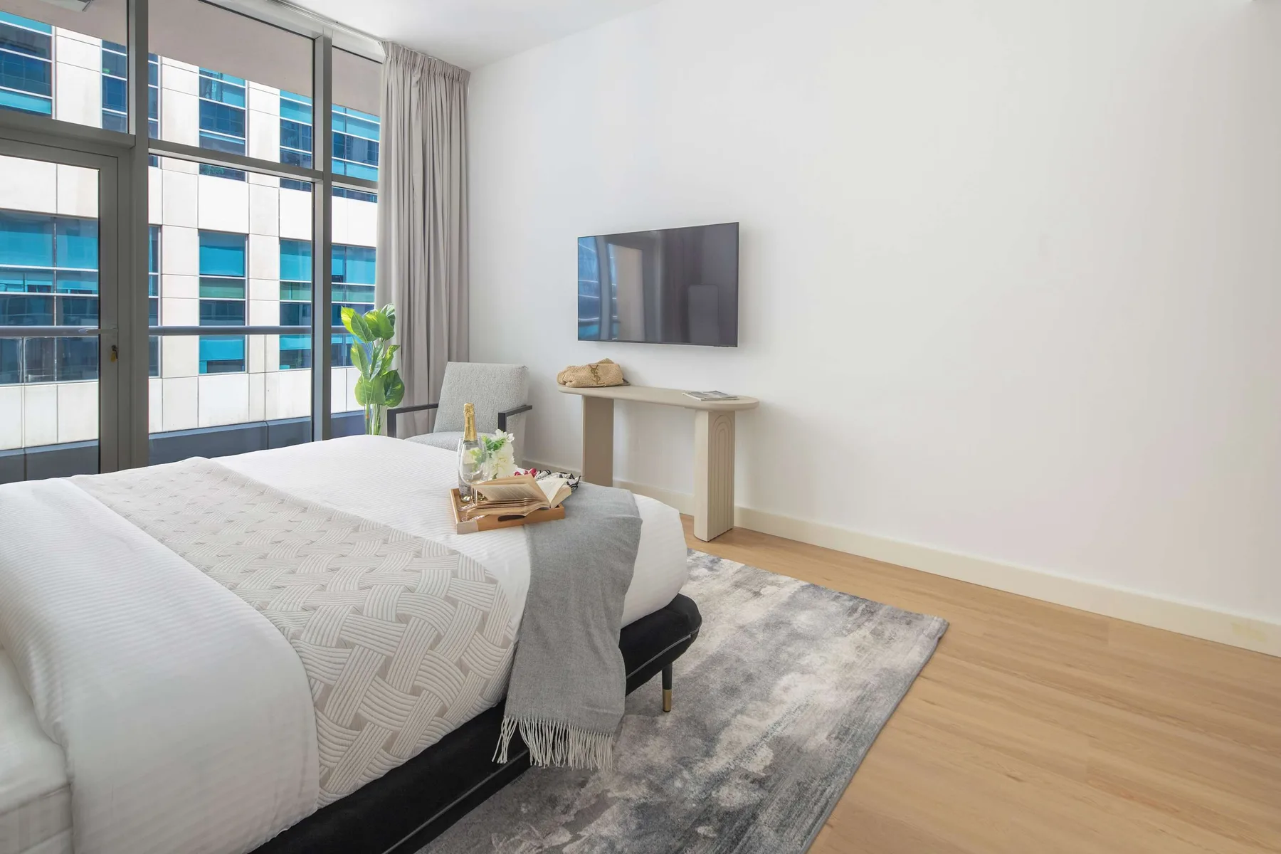 A bright bedroom with a neatly made bed beside large windows.