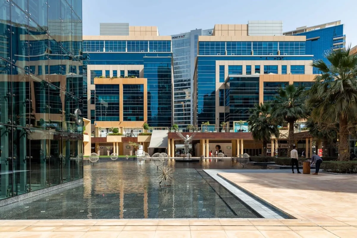 A modern glass office complex surrounds a shallow reflecting pool and paved courtyard.