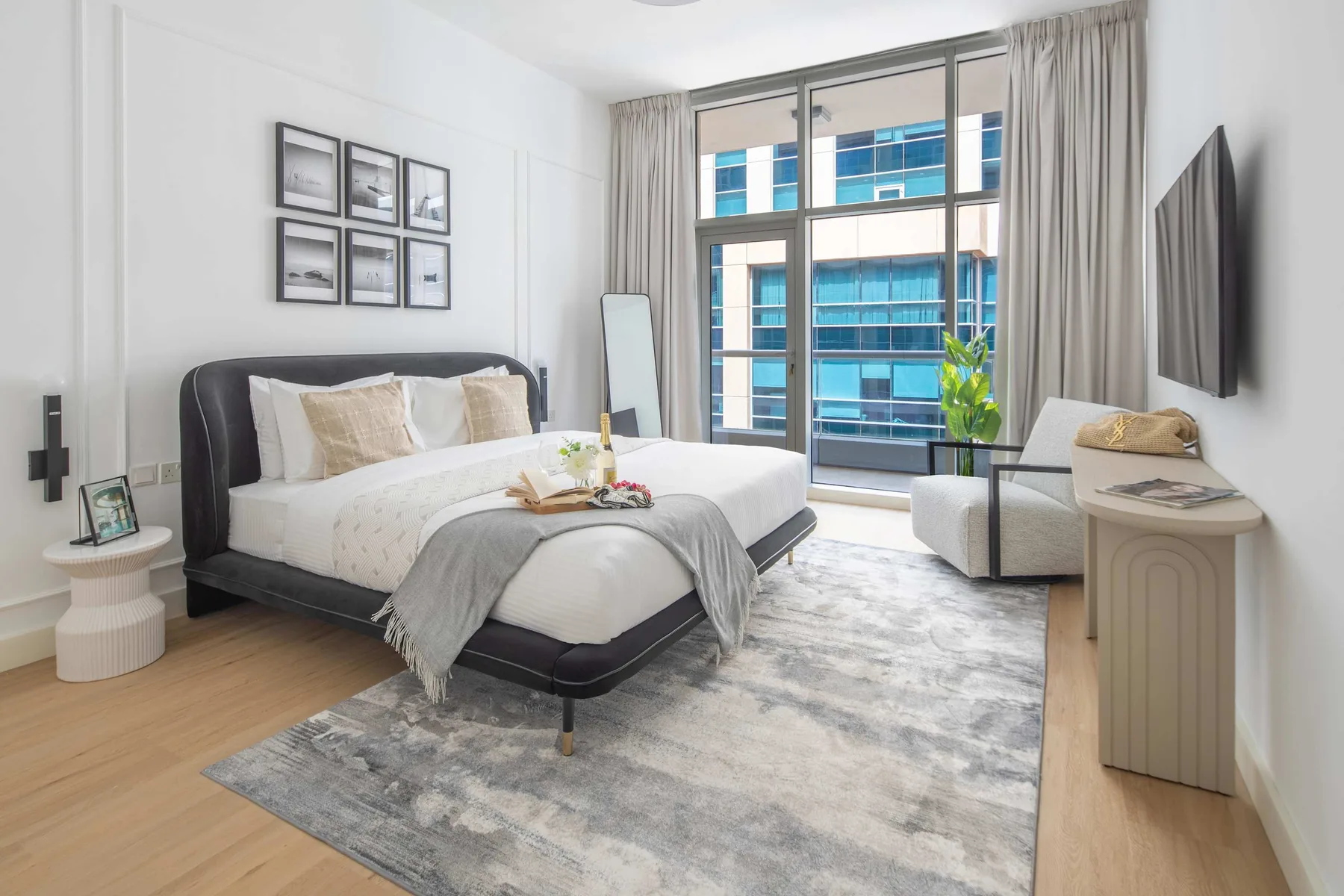 A bright bedroom with a large bed, a seating area, and tall windows.