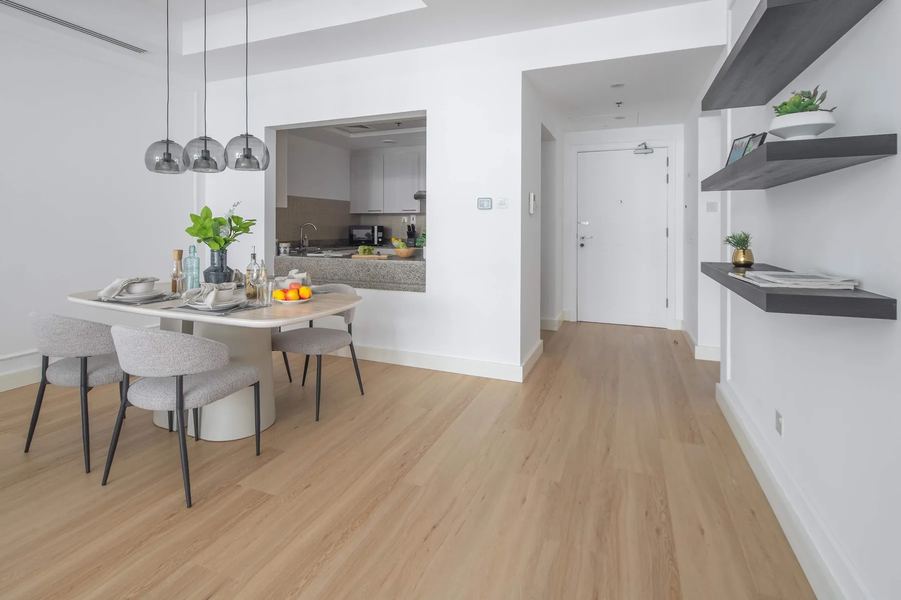 An open dining area with a set table beside a kitchen pass-through and hallway.