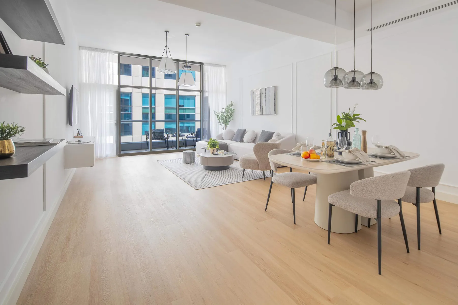 Una sala de estar y comedor diáfana con grandes ventanas y muebles claros.