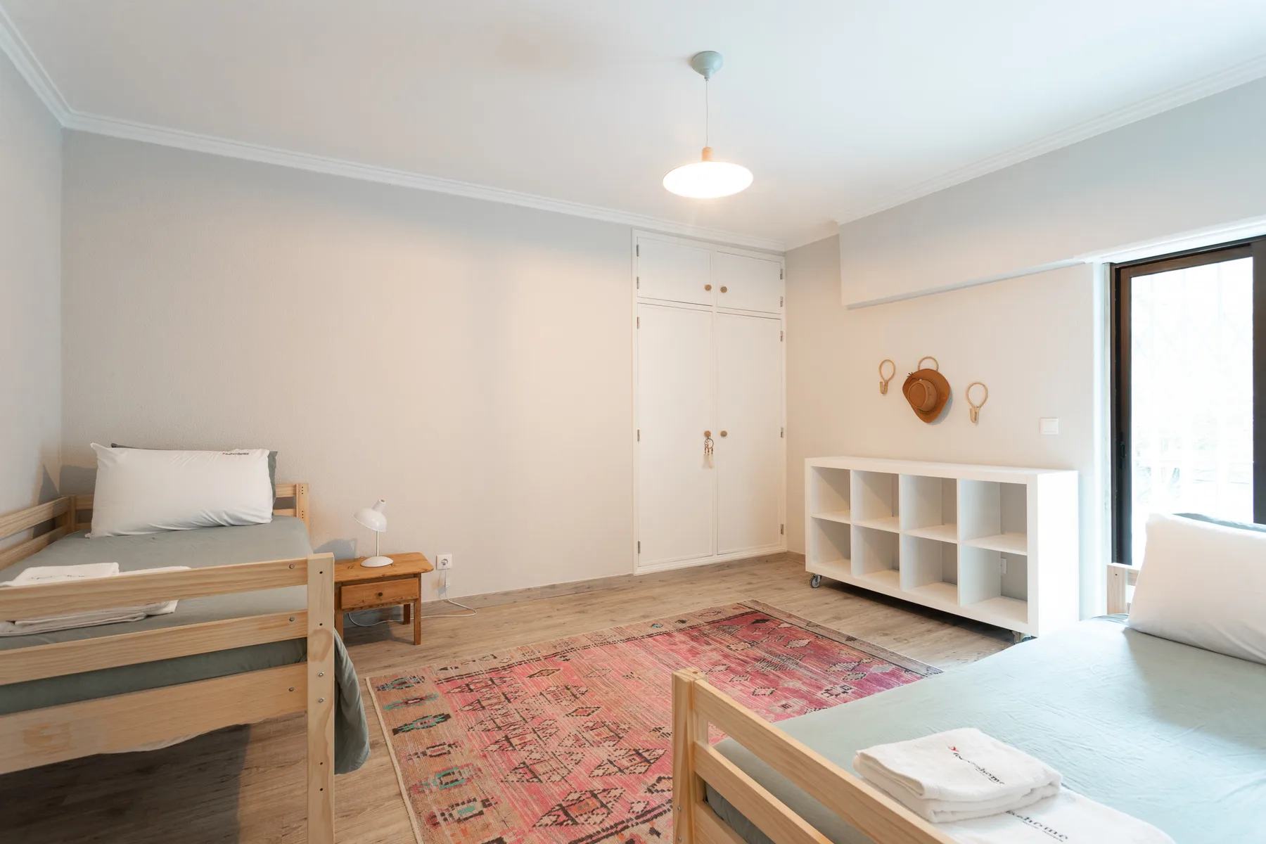 A bright bedroom with wooden beds, a patterned rug, and a low storage unit.
