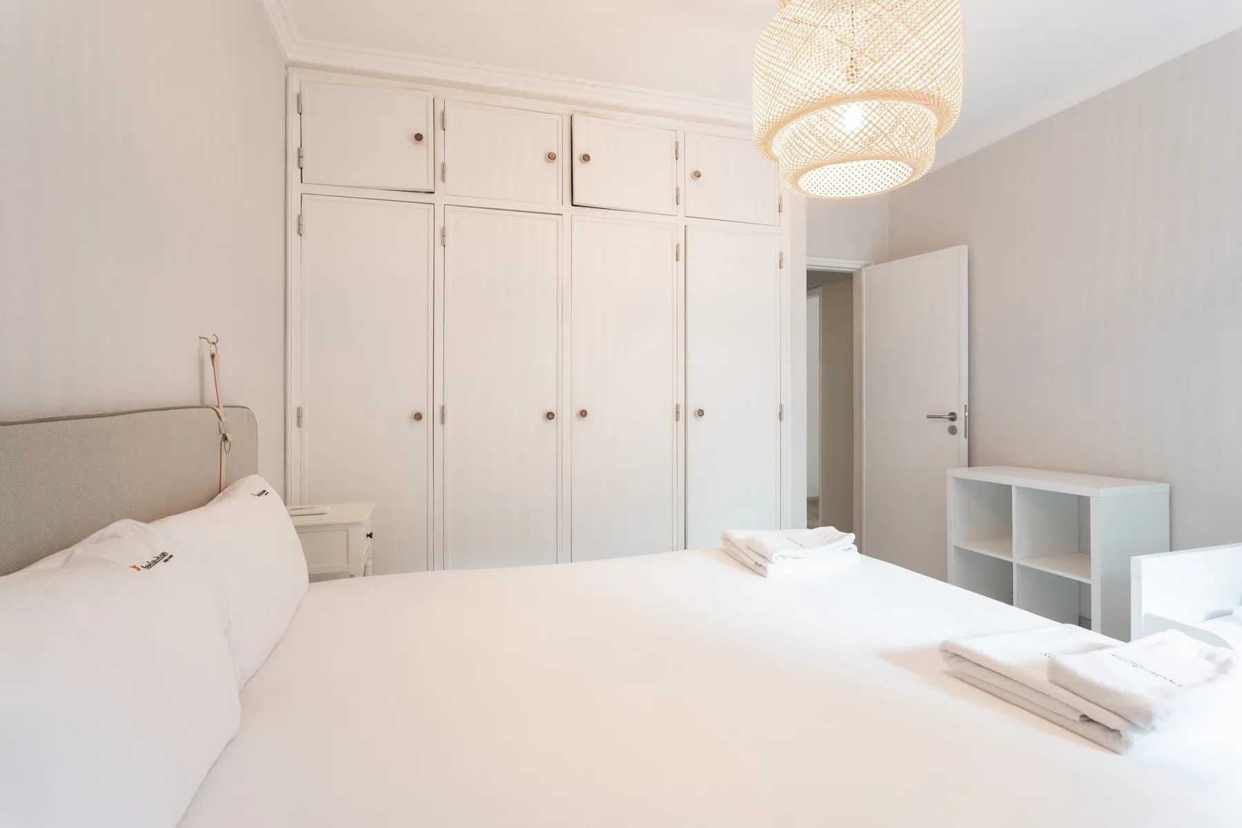 A bright bedroom with a white bed, built-in wardrobes, and an open door.