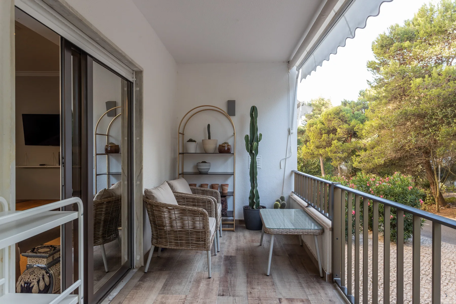 A covered balcony with wicker seating and trees visible beyond the railing.