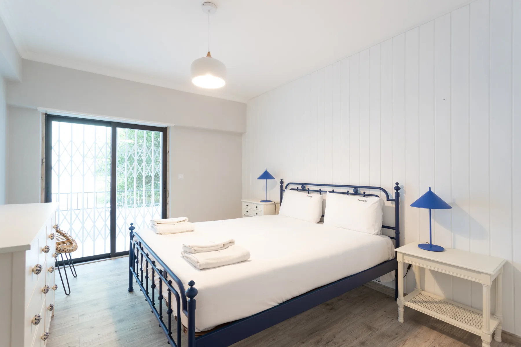 Un dormitorio luminoso con cama doble, lámparas azules y una puerta corrediza de vidrio.
