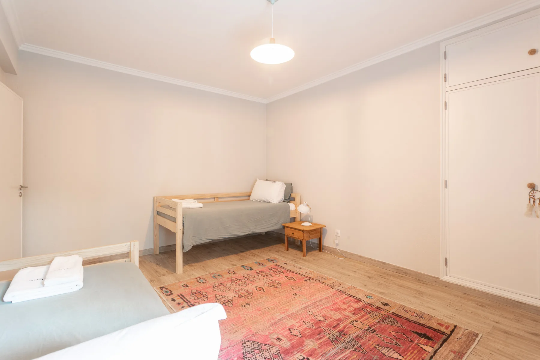 A bedroom with two beds, a wooden bedside table, and a patterned rug.