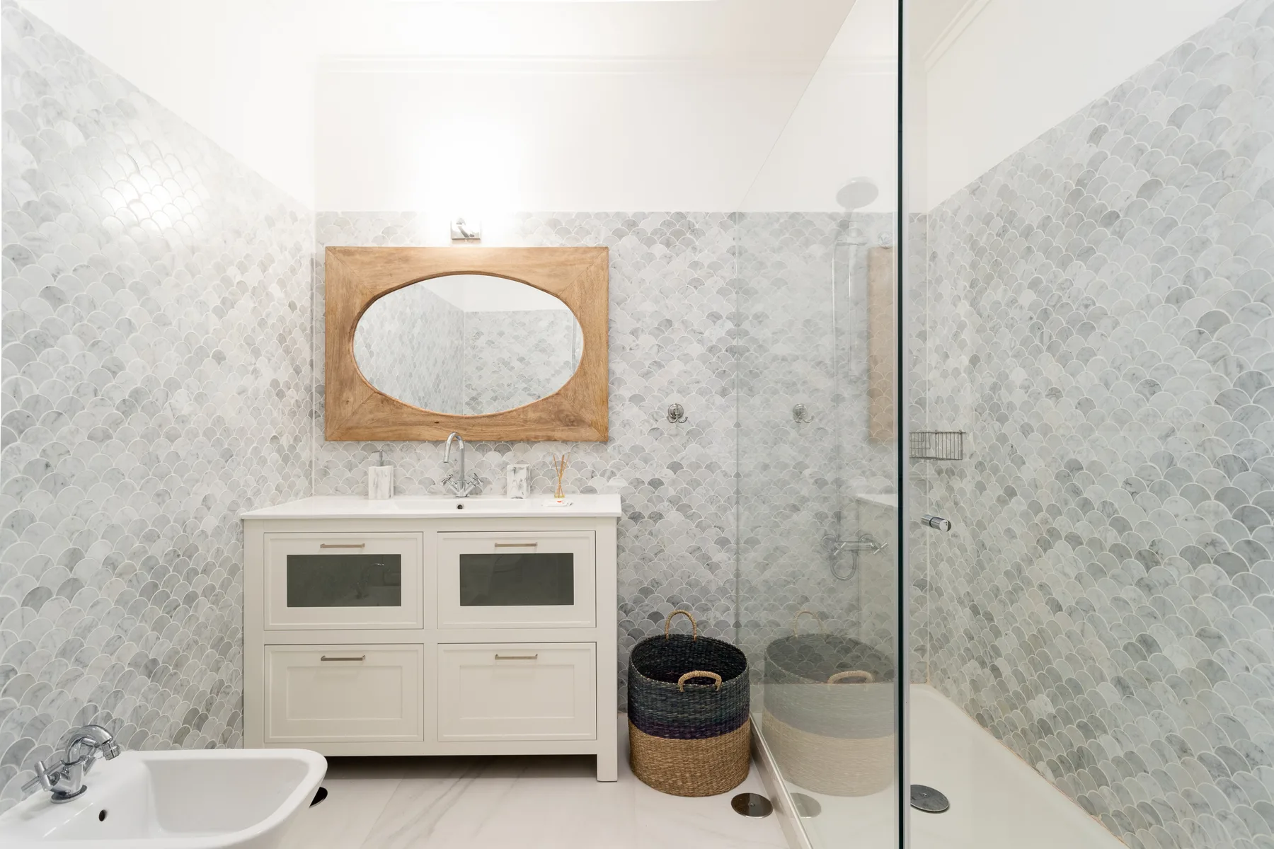 A bright bathroom with a vanity, oval mirror, and glass shower.