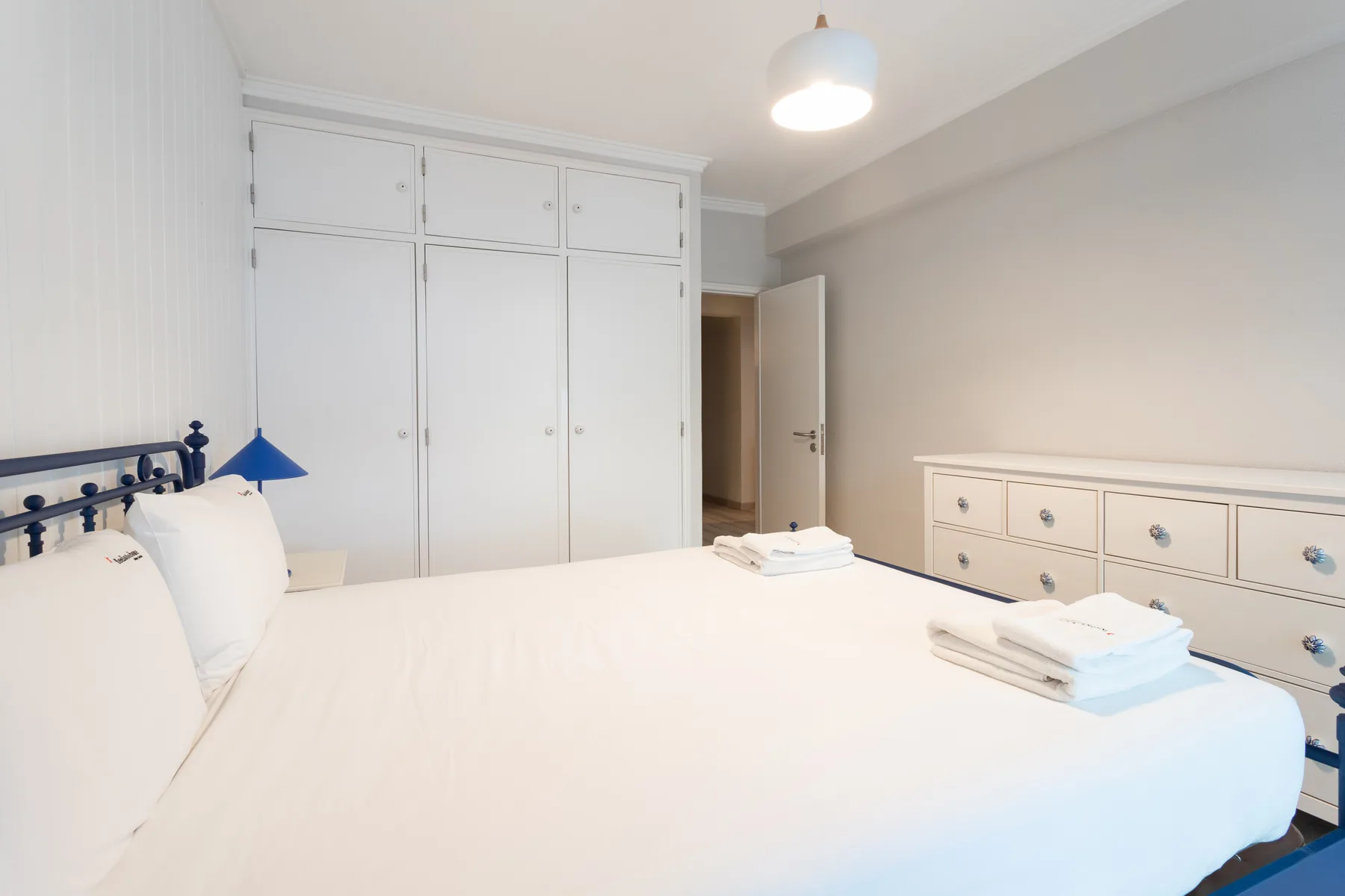 A bright bedroom with a large bed, white wardrobes, and a dresser.