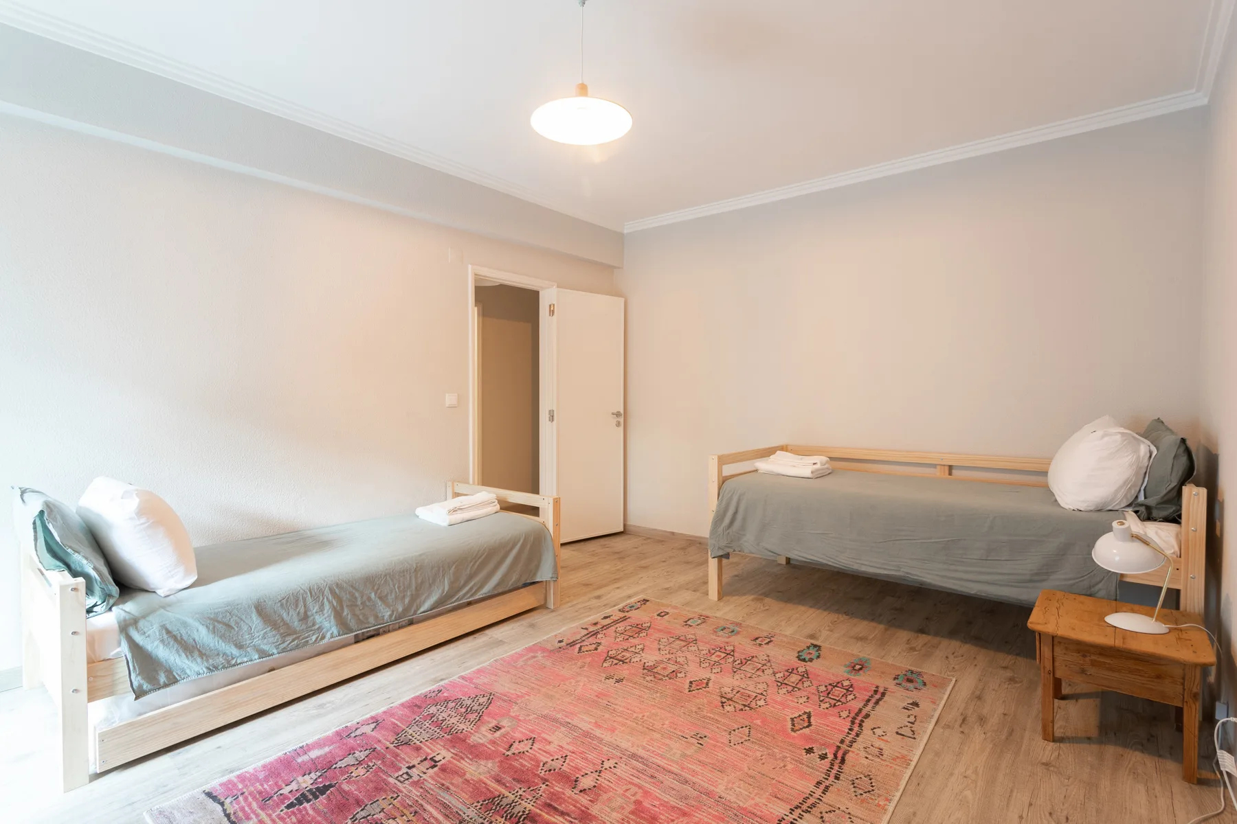 A bedroom with two single beds, a patterned rug, and a bedside table.