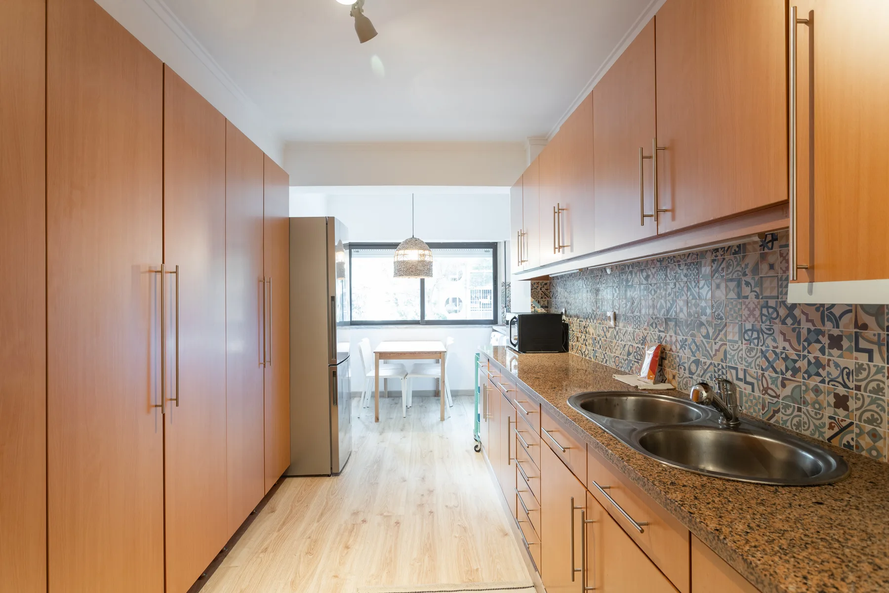 A galley kitchen with wooden cabinets, patterned backsplash, and a double sink.