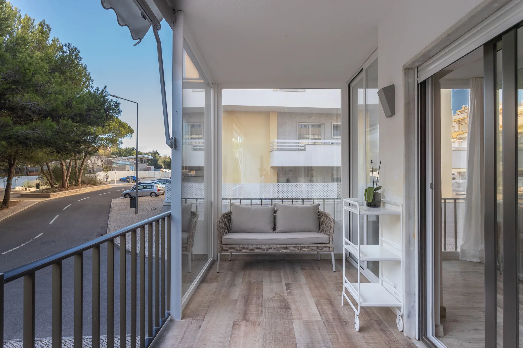 A covered balcony with a seating area overlooks a tree-lined street.