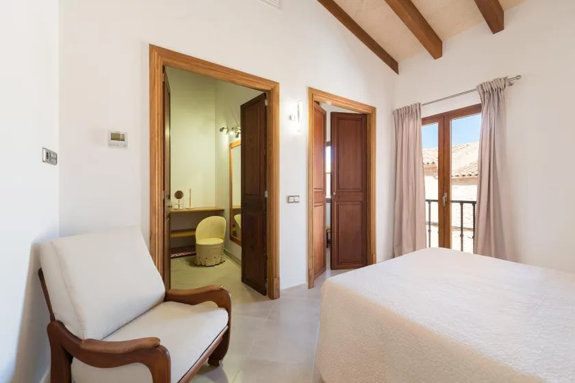 A bedroom with a bed, an upholstered chair, and doors opening to a balcony.