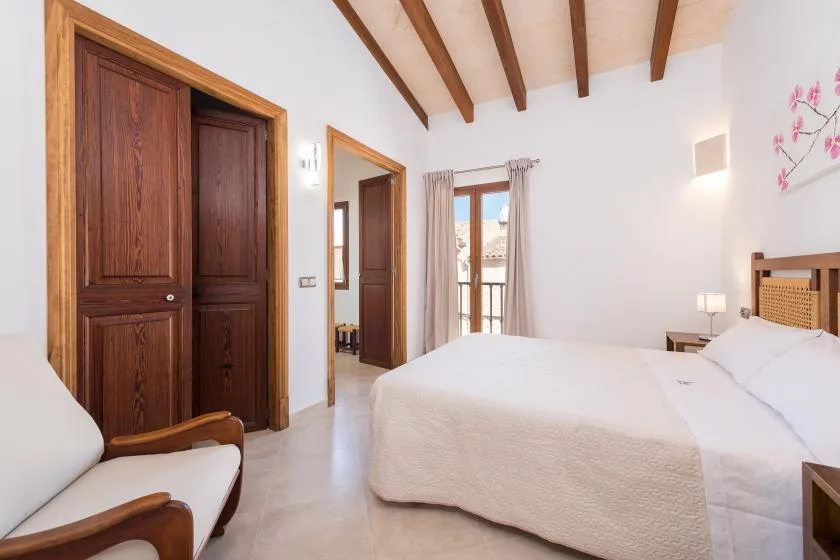A bright bedroom with a bed, wooden doors, and exposed ceiling beams.